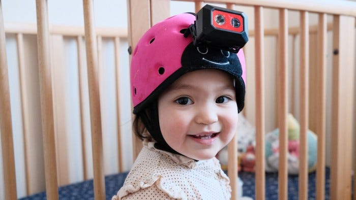 A smiling 18-month-old baby girl wearing a head-mounted camera