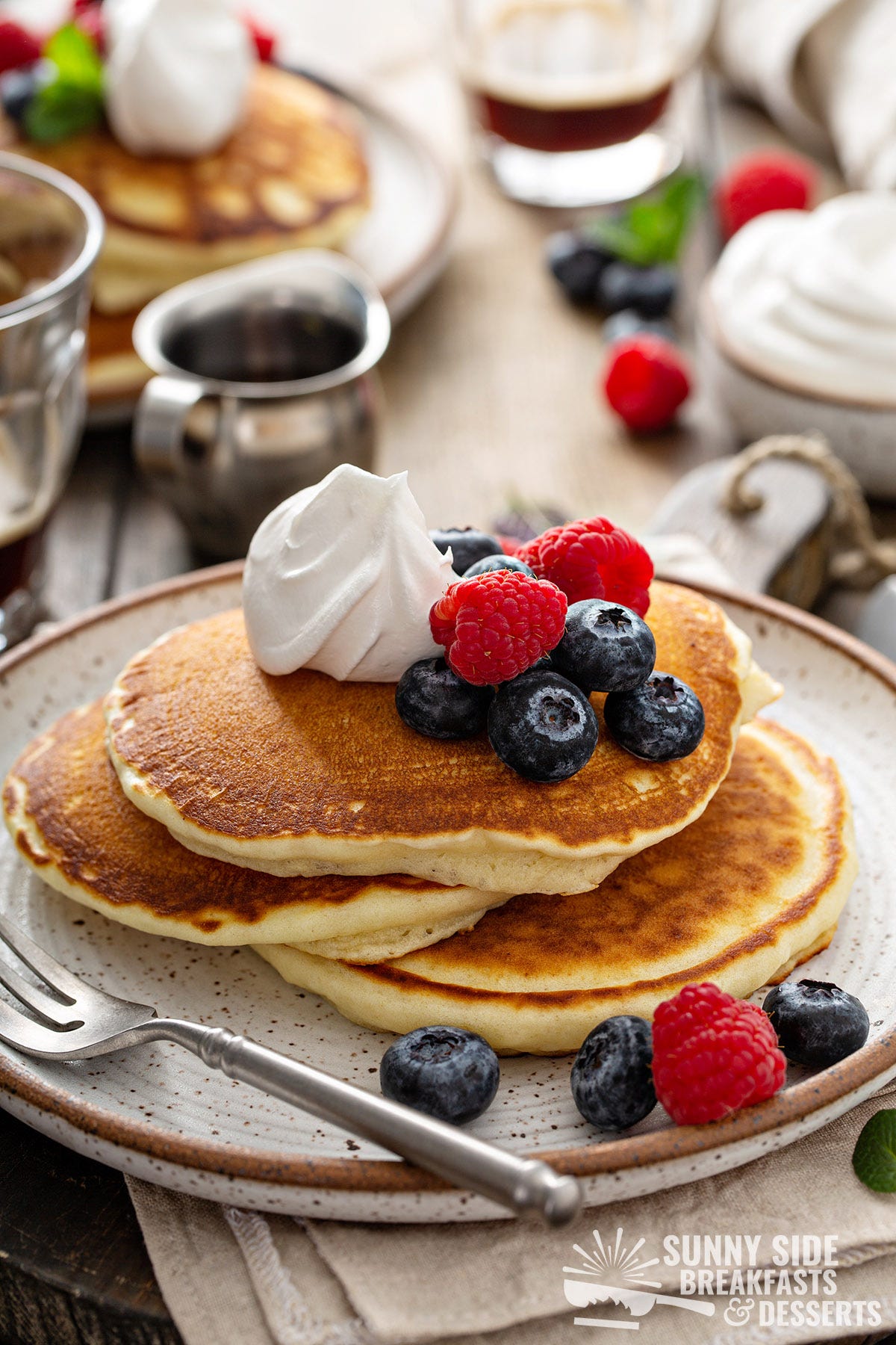 Stack of pancakes with whipped cream and berries.