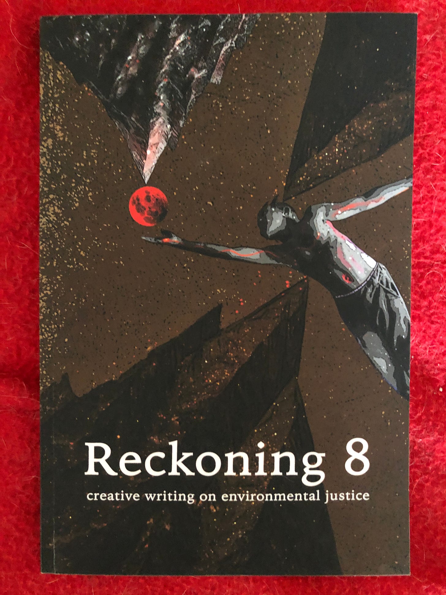 Brown cover with a figure reaching for a blood red sun, RECKONING 8, creative writing on environmental justice