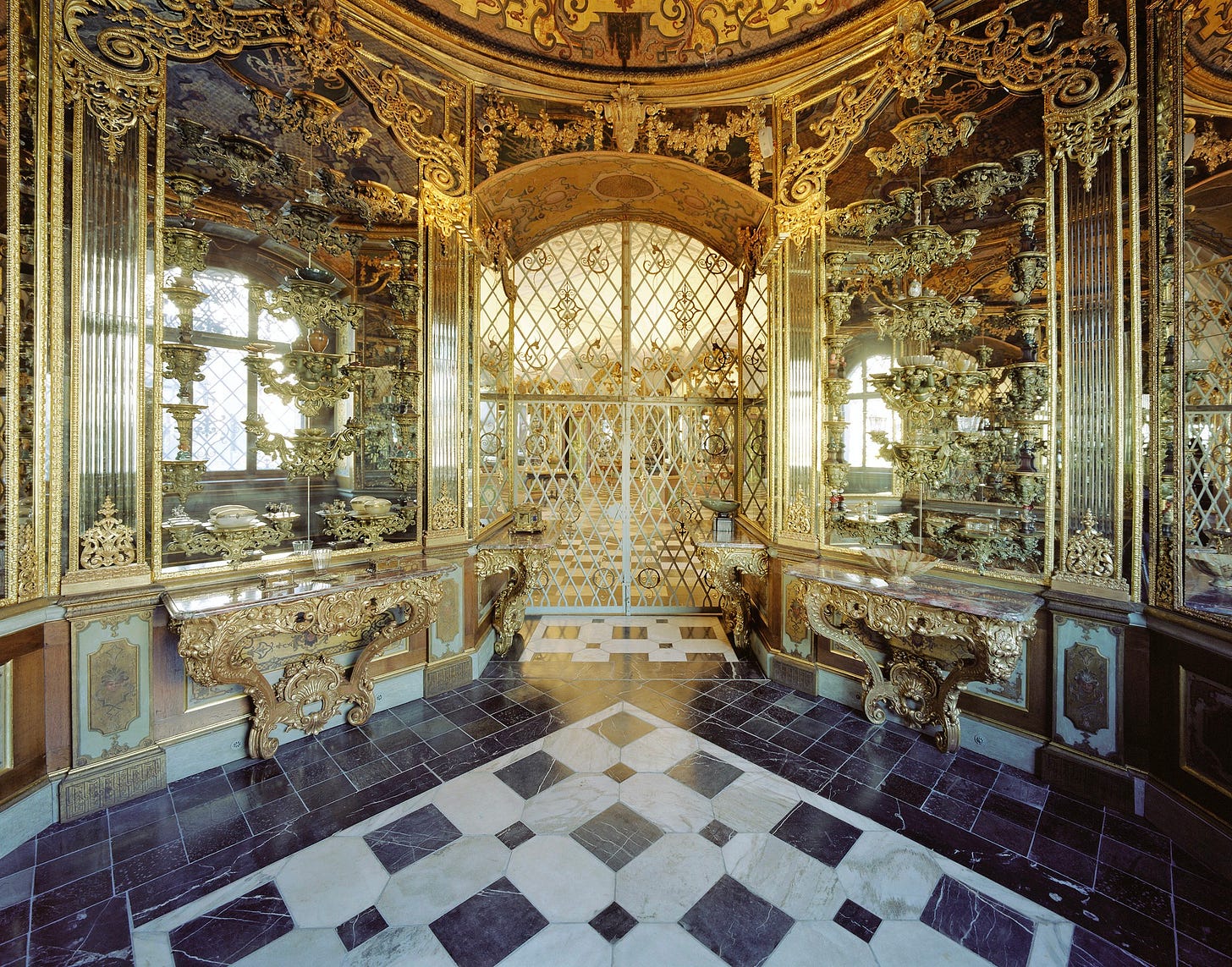 Two mirrored walls and a gated archway covered in mirrors and ornate gold decorations.