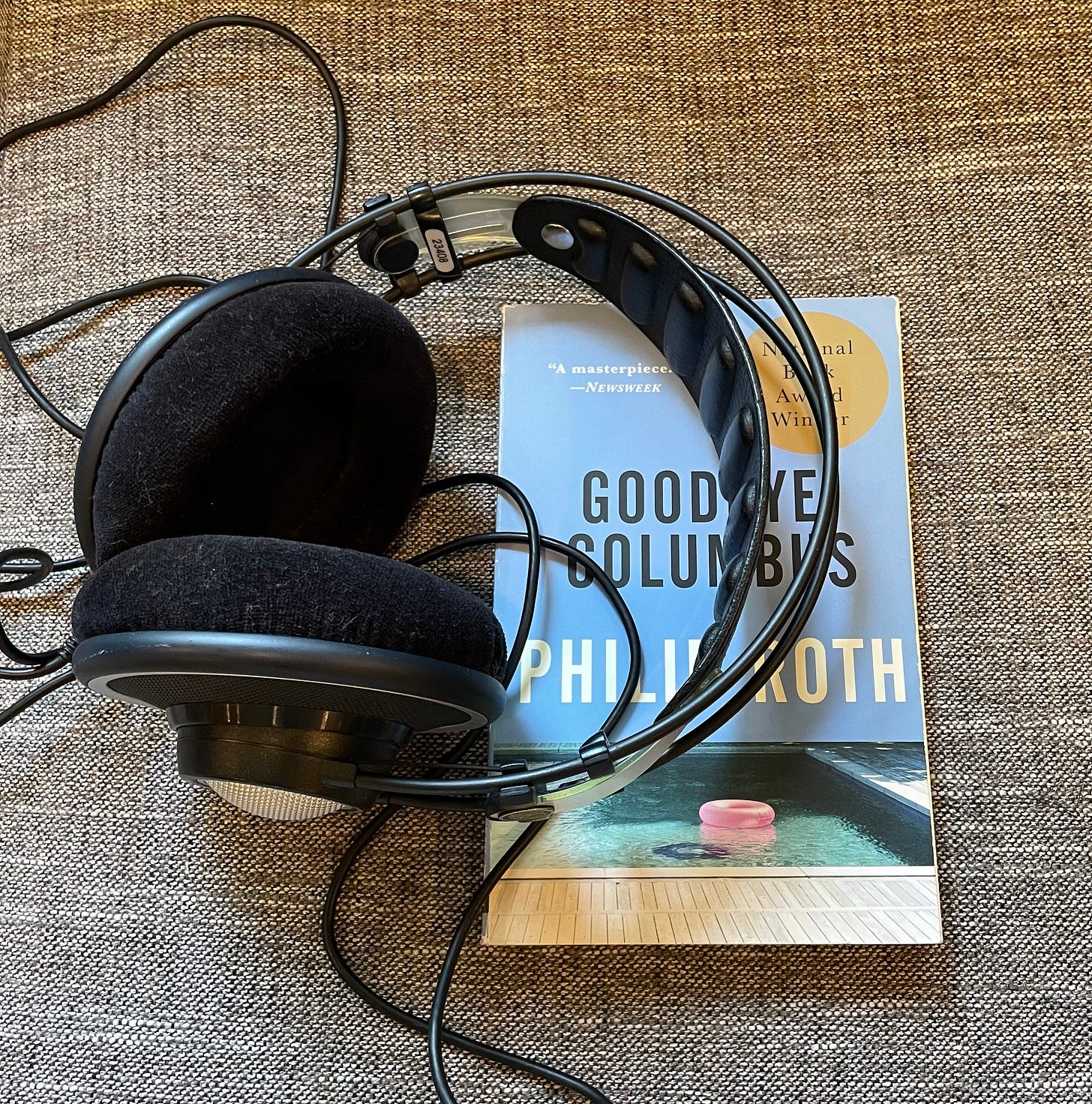 A pair of large headphones rests on top of a paperback copy of Goodbye, Columbus by Philip Roth