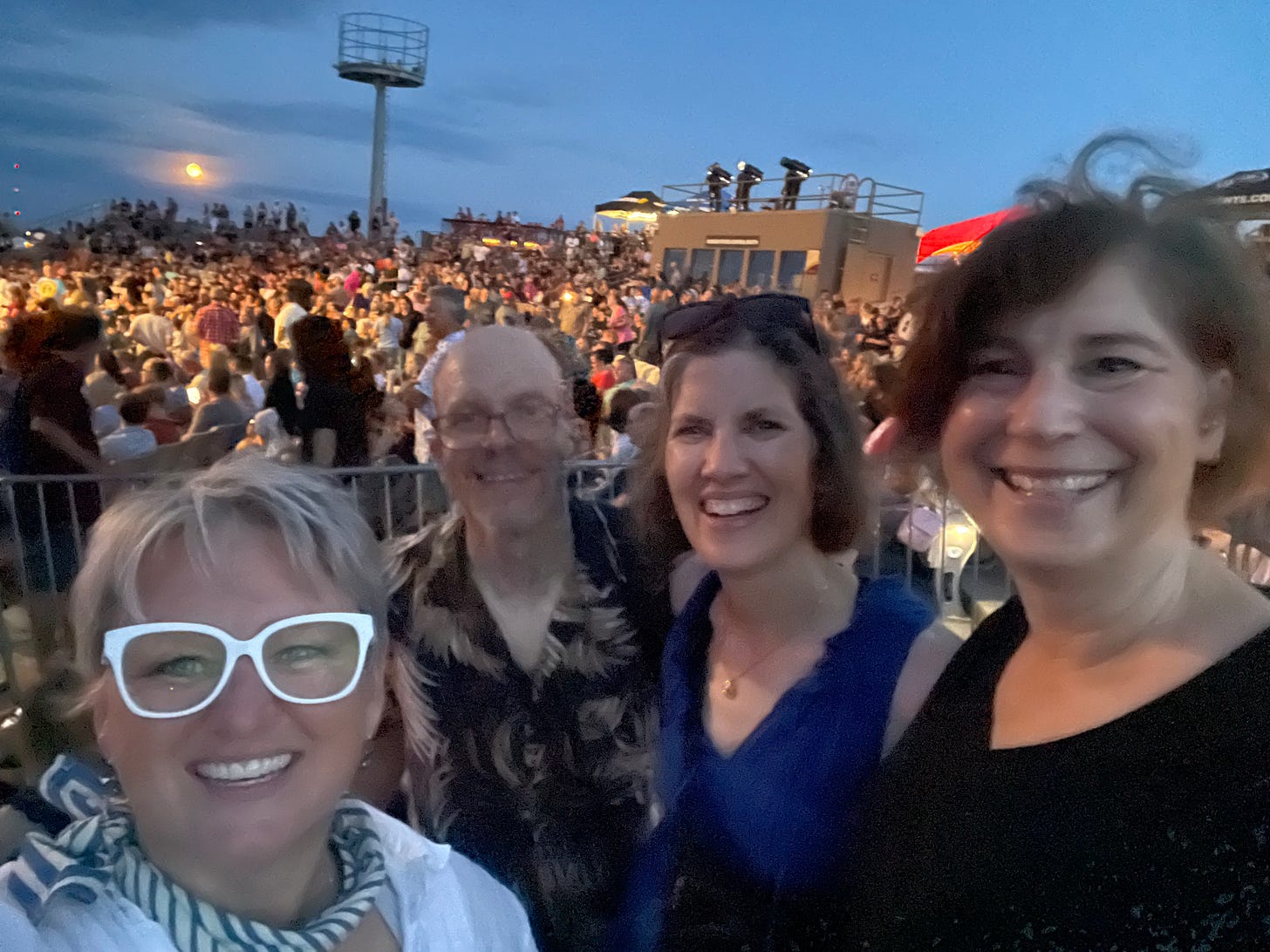 Four friends smile in the midst of a crowd of music lovers as the full moon rises