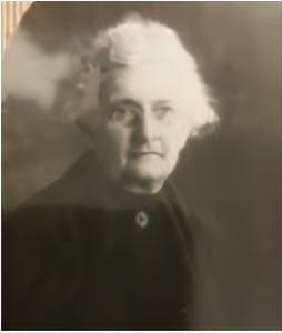 Studio photo of an older woman with white hair and a dark jacket.