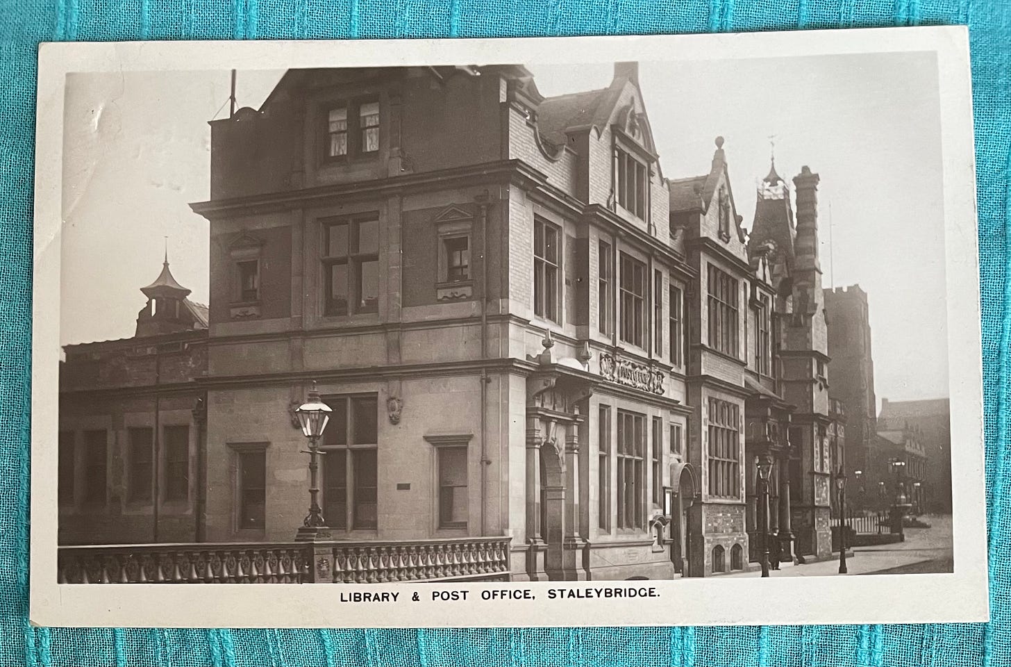 A sepia postcard showing solid looking late 19th century buildings, captioned Library and Post Office Stalybridge.