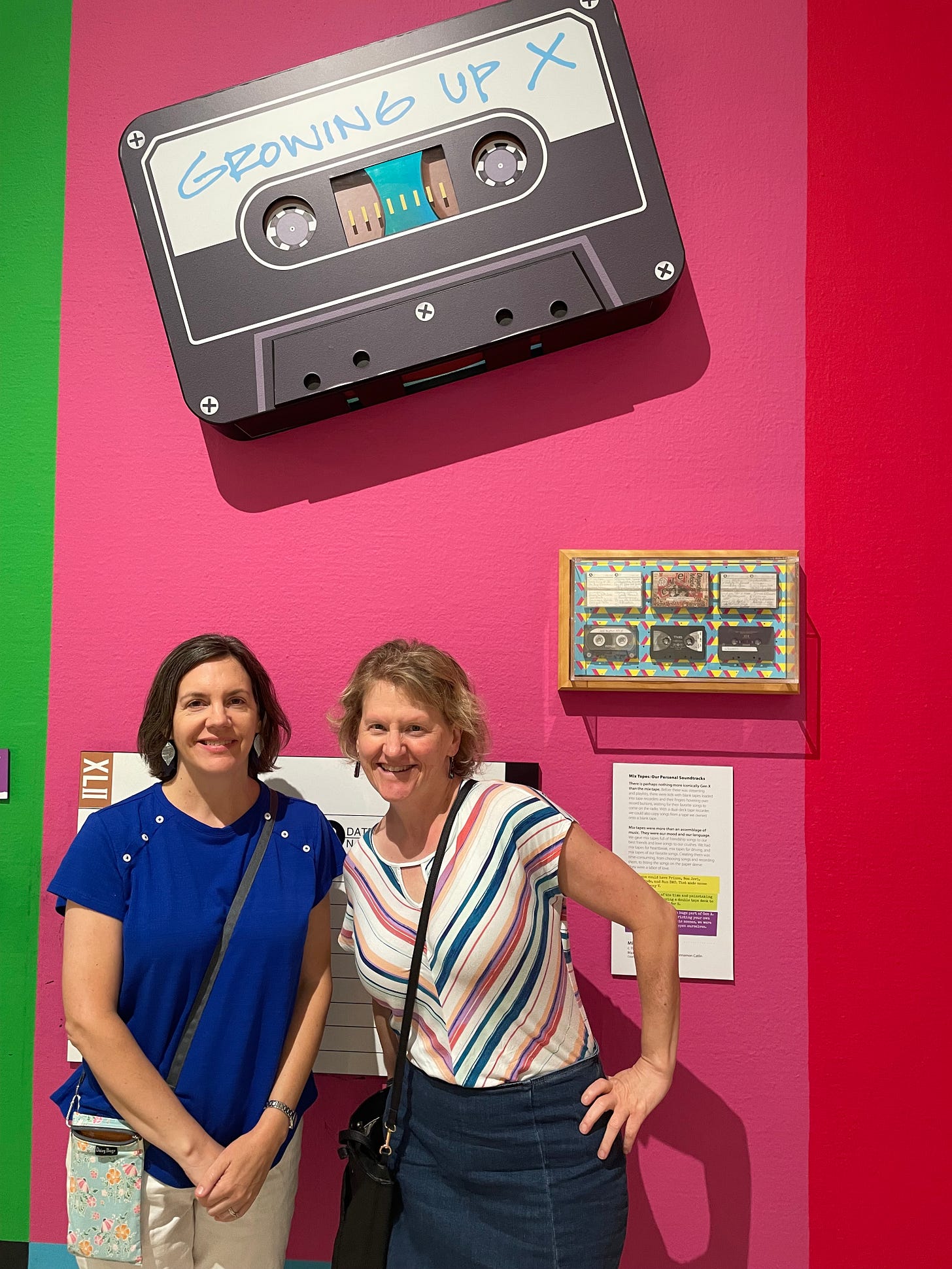 photo of two sisters standing in front of a large image of a cassette tape