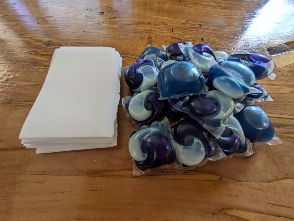 a pile of white paper-like sheets next to a mound of blue and white detergent pods on a coffee table