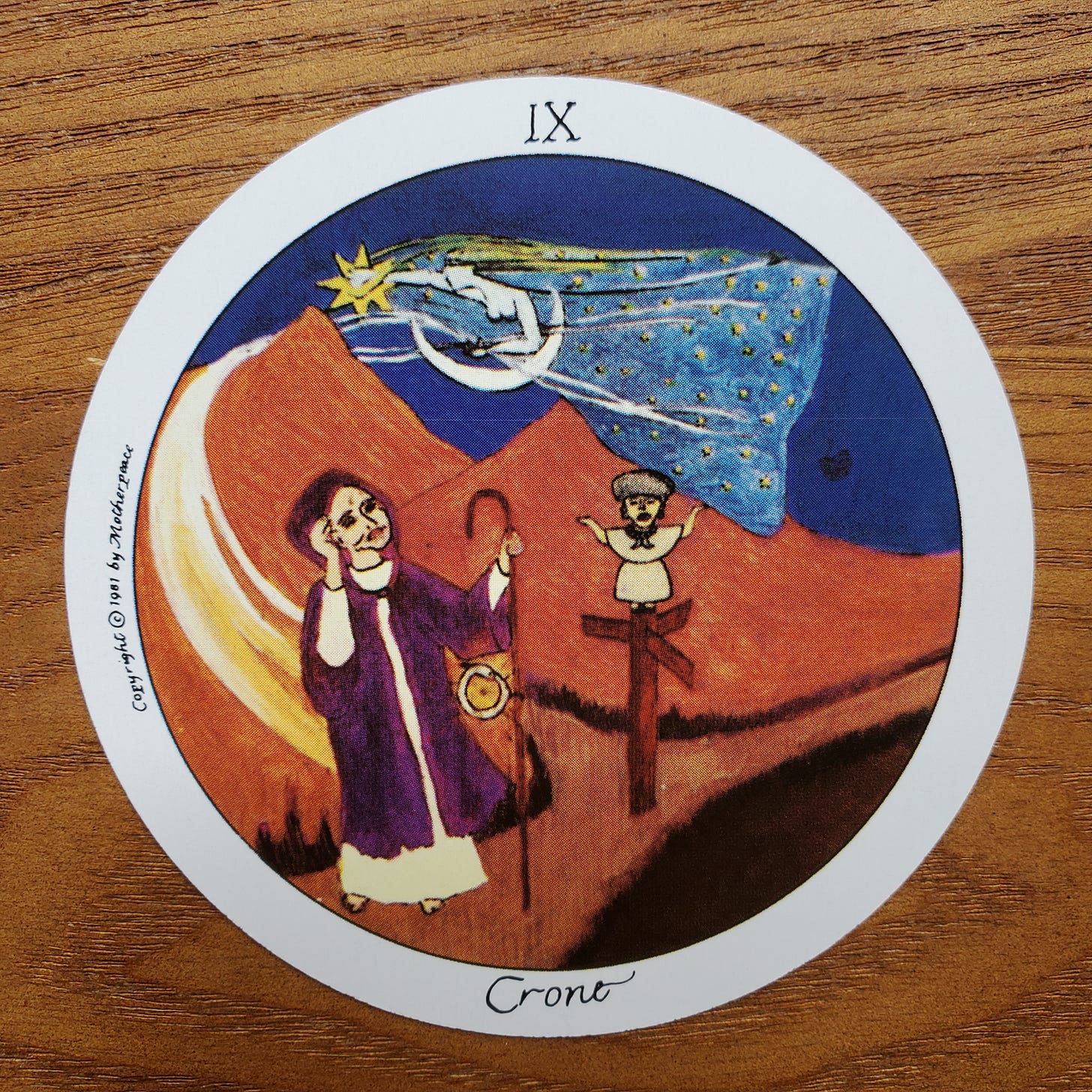 A round card with the roman numeral 9 and the word crone in the border around the card. Inside the border, an image of a older woman with a walkig staff an angle flying overhead, and another small female figure perched atop a crossroads sign.