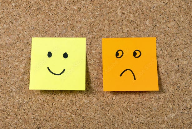 Two sticky notes: One with a smiley face (left) and one with a sad face (right); stuck to cork board.