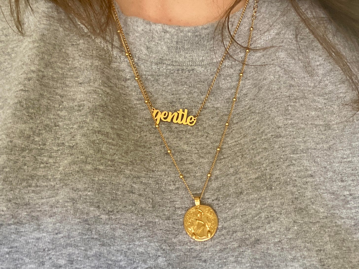 a photo of my chest wearing a gray sweatshirt with two gold necklaces. one says gentle and one is gold coin.