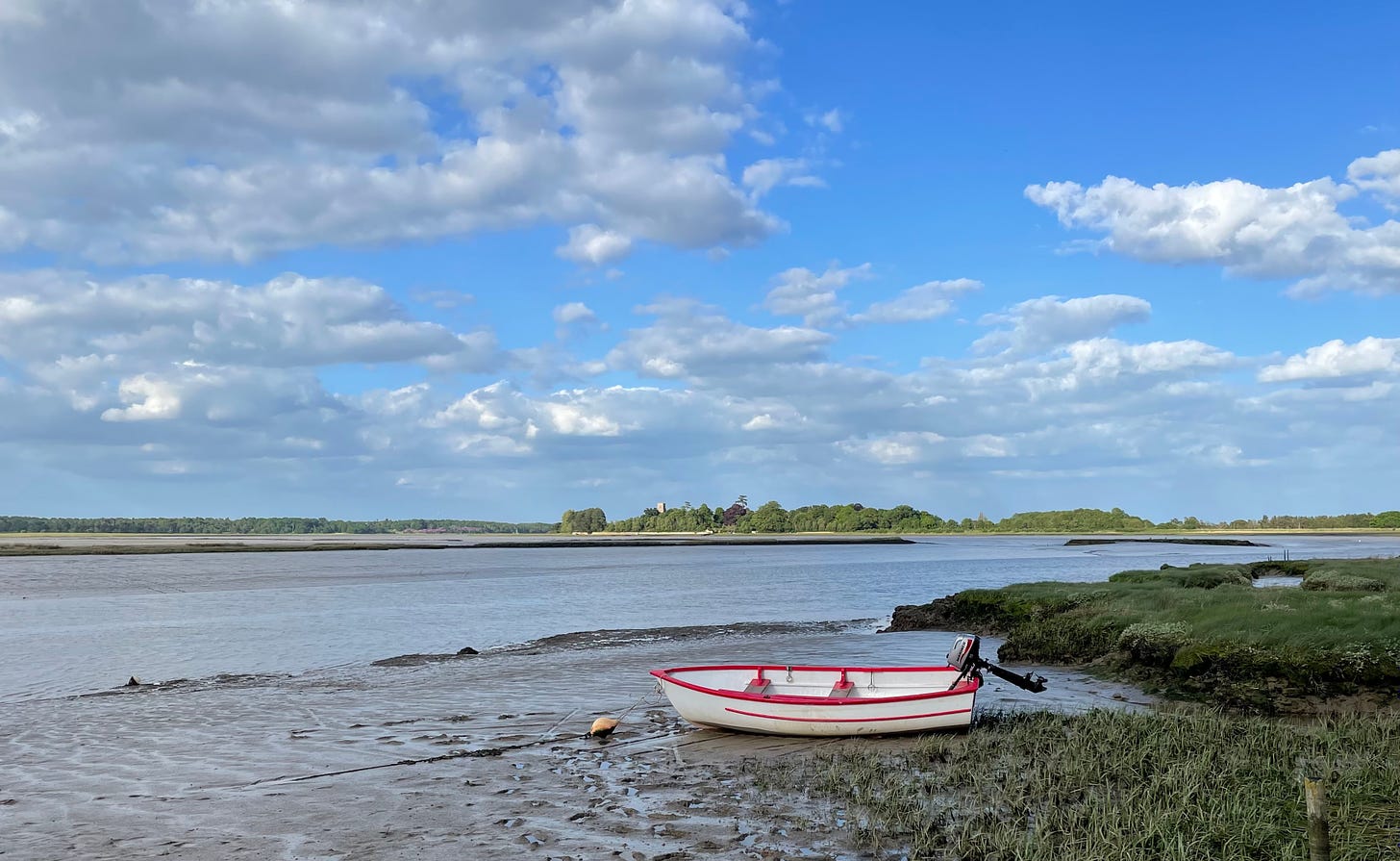 Looking towards St Botolph Iken situated on the only raised spit of land in an otherwise flat landscape with a red and white rowing boat in the foreground