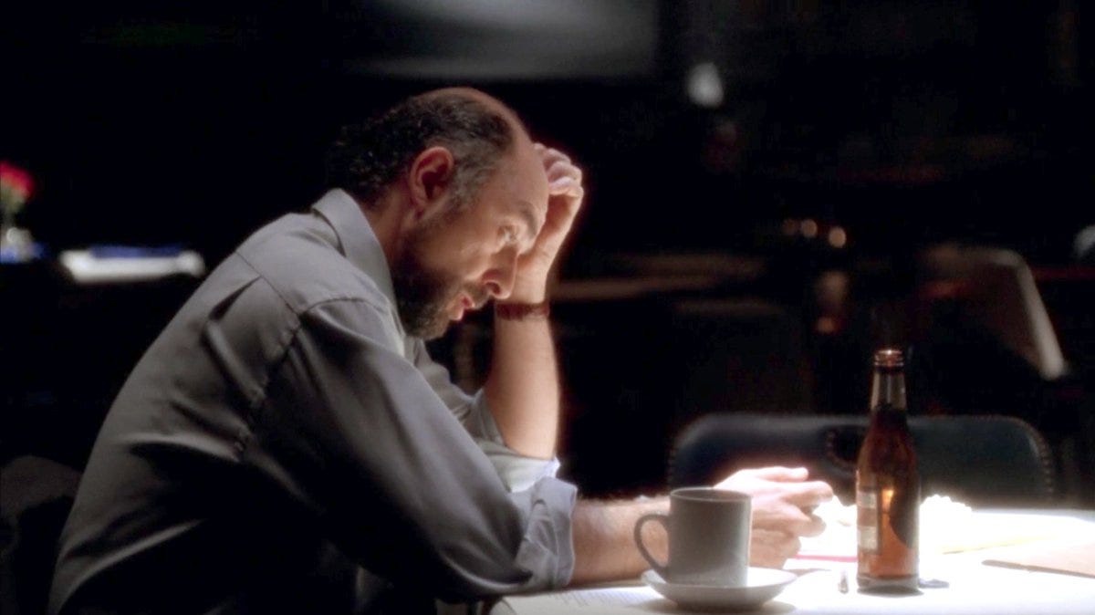 West Wing screenshot: Toby Ziegler sitting over some papers with both beer and coffee, looking lost and frustrated
