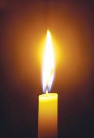 An image of a single lit candle glowing yellow in the dark.