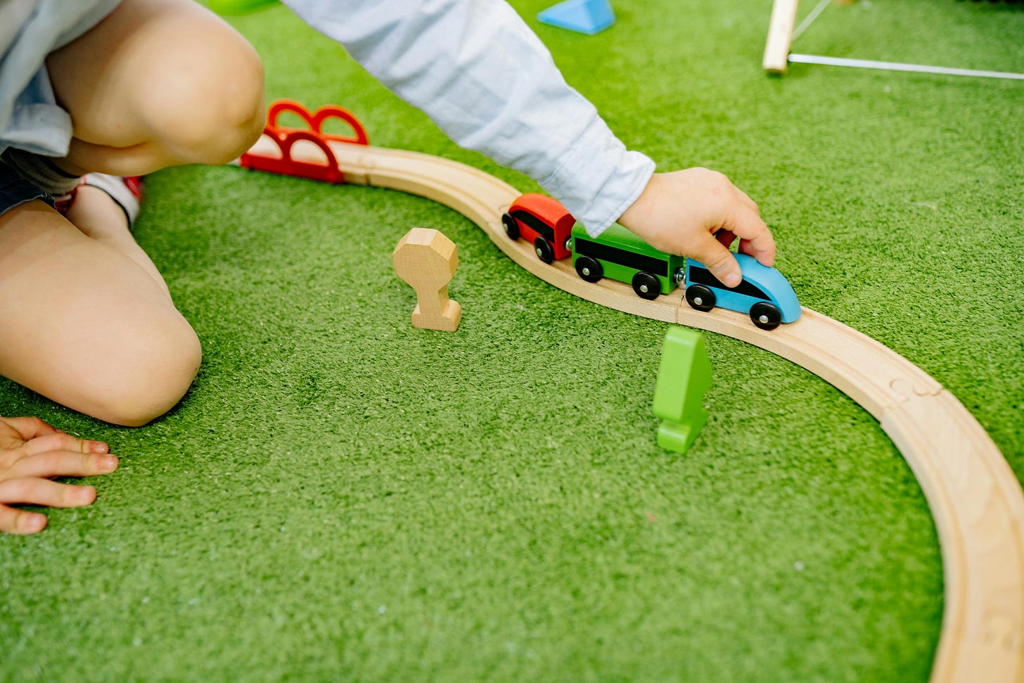 Child seated on lawn pushing colorful train on wooden track