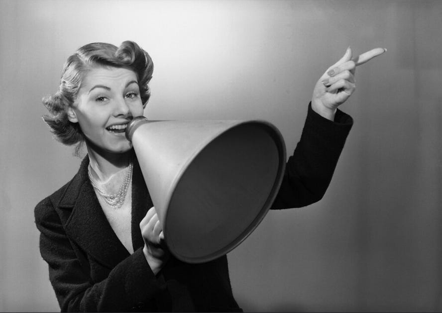 Black and white photo of a woman holding a loudhailer to her mouth and pointing