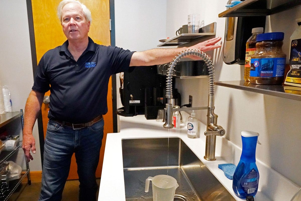 A man points at the wall over a dripping kitchen sink