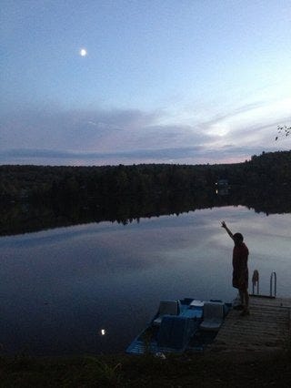 David Graeber standing beside lake at dusk pointing to moon in the sky