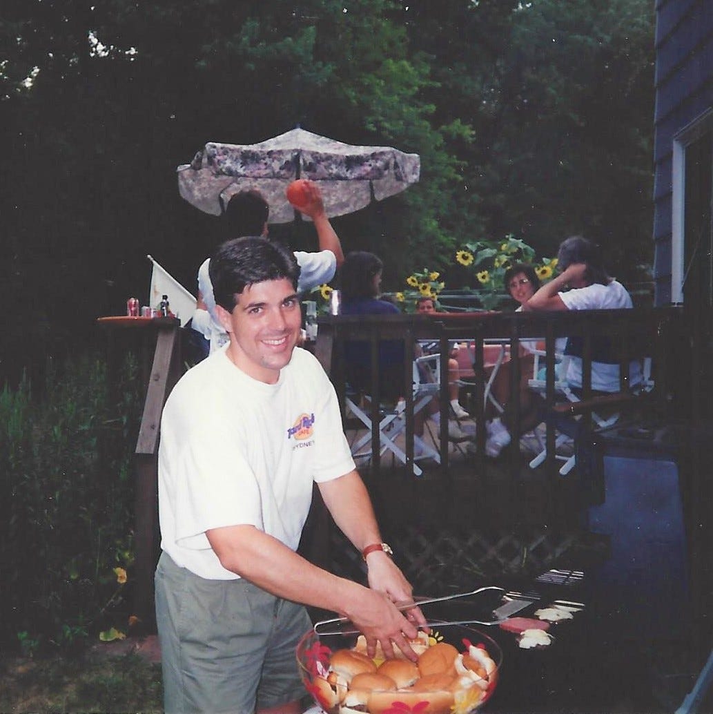 20-something man cooks burgers on the grill for a gathering of his friends
