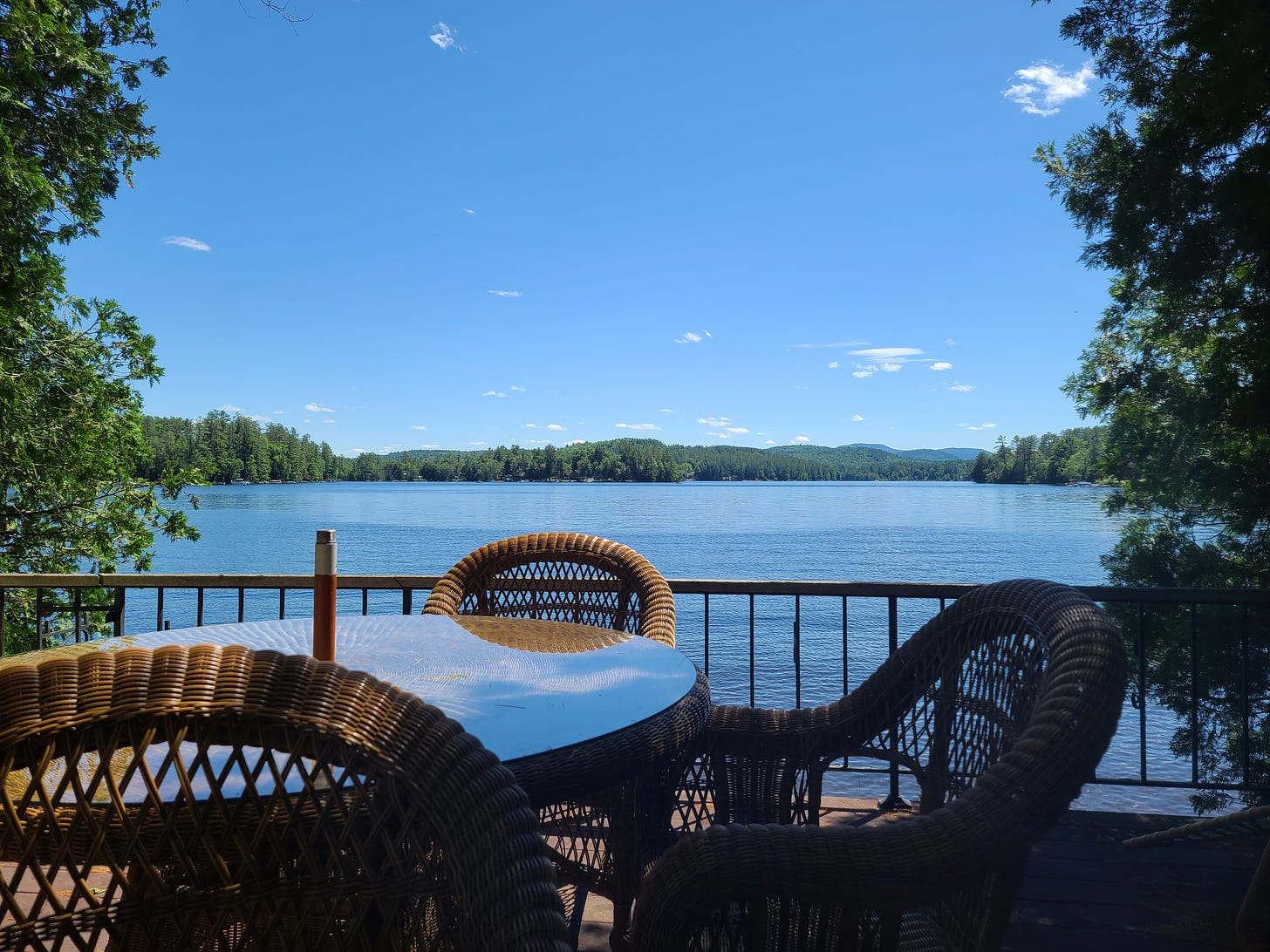 A photo of a deck over a lake with trees flanking it under a blue sky.