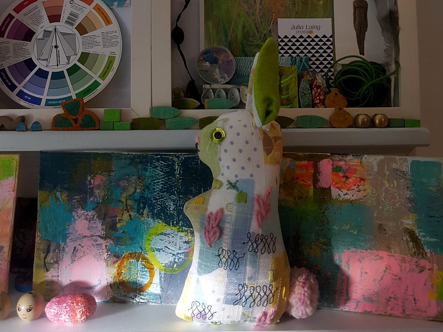 Studio shelves with handmade textile rabbit doll and paintings in progress by Julia Laing