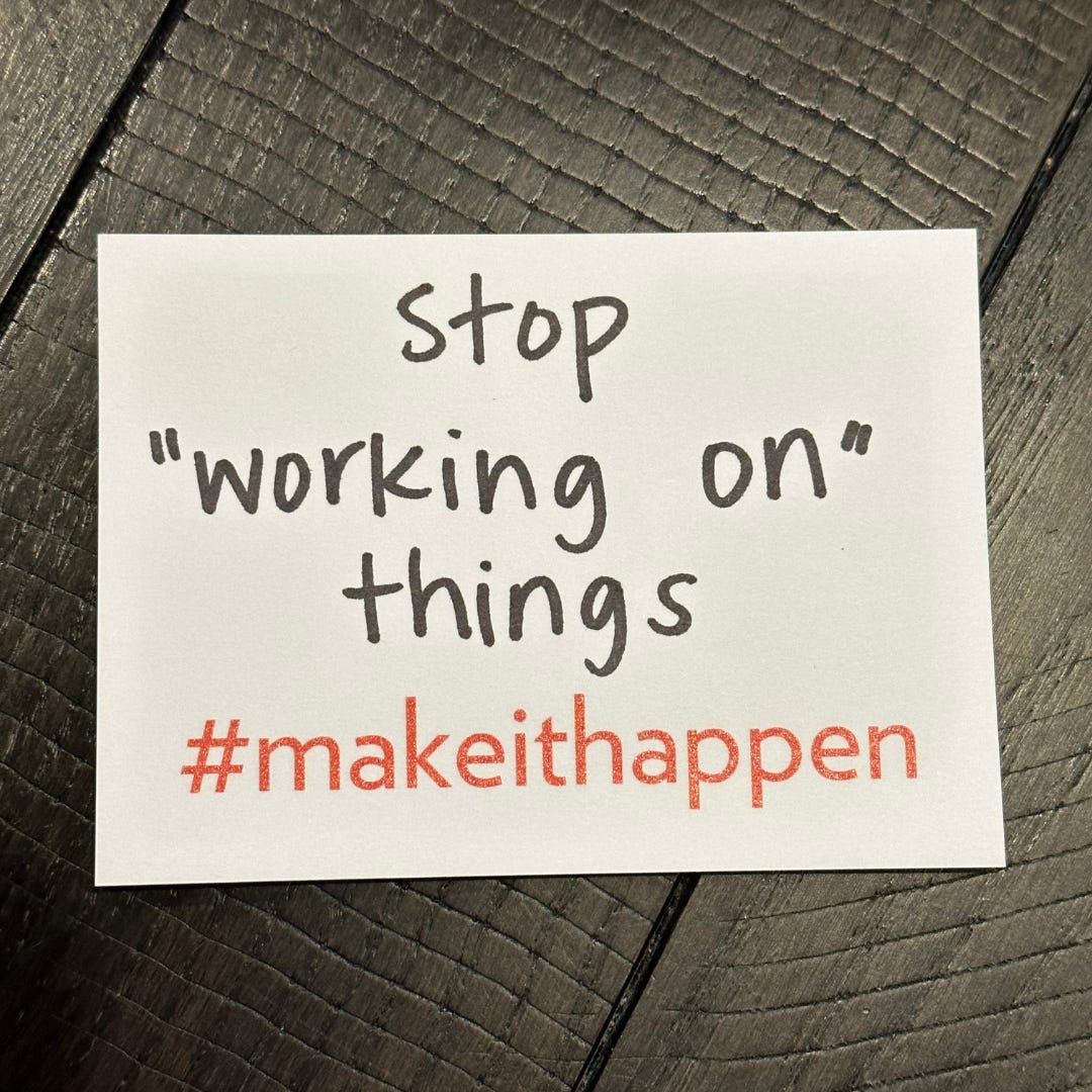 a photo of a sticky note that has, “stop ‘working on’ things” written on it and includes #makeithappen preprinted on the bottom