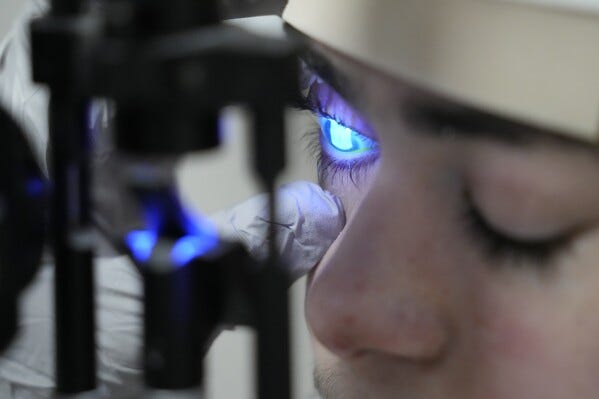 Dr. Alfonso Sabater, checks Antonio Vento Carvajal's eye under a blue light after applying a stain to check to see if more ulcers had developed, before a gene therapy treatment, Thursday, July 6, 2023, at University of Miami Health System's Bascom Palmer Eye Institute in Miami. Antonio was born with dystrophic epidermolysis bullosa, a rare genetic condition that causes blisters all over his body and in his eyes. He was blind for much of his life but can see again after getting gene therapy eyedrops. (AP Photo/Wilfredo Lee)