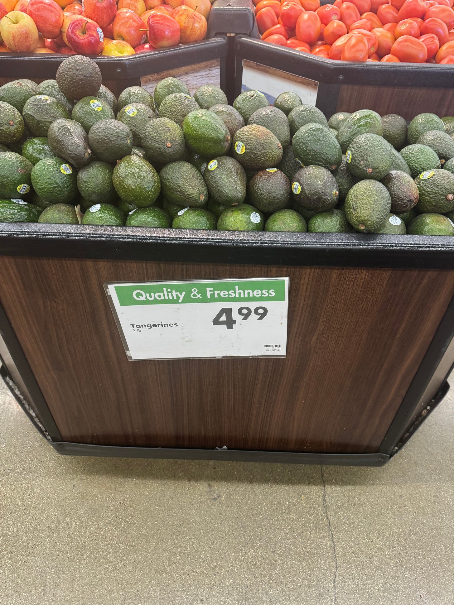 A display of avocados in a grocery store but the sign says "tangerines" 