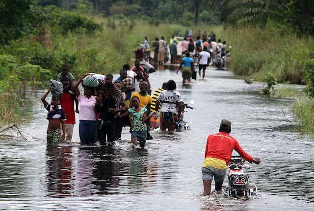 People carrying their belongings through a flooded green landscape in Nigeria