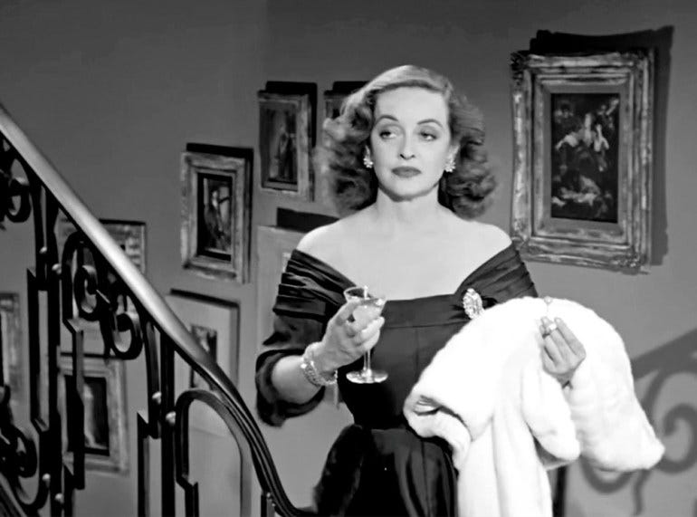 Bette Davis as Margo Channing in the movie All About Eve. She is in an evening gown, holding a martini glass and a fur stole, and wearing a wry expression.