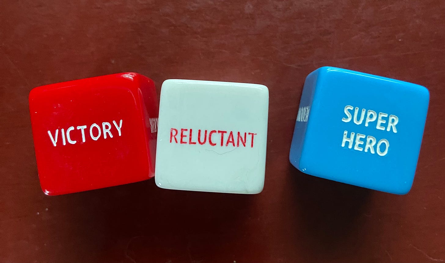 A red dice that says, VICTORY, a white dice that says RELUCTANT, and a blue dice that says SUPER HERO