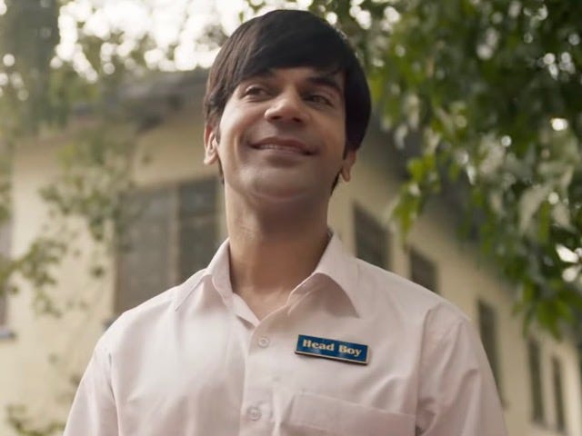 A still from Hindi film, 'Srikanth'. Bust shot of a grinning Srikanth played by Rajkummar Rao, in a white school shirt with a 'Head Boy' badge.
