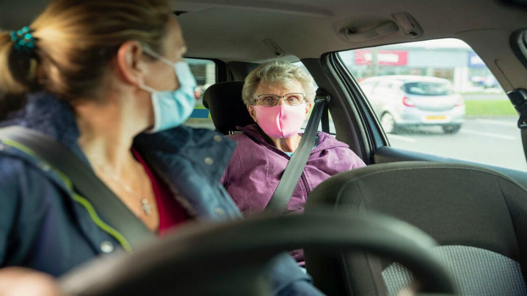 masked woman driving an older woman who has a mask on