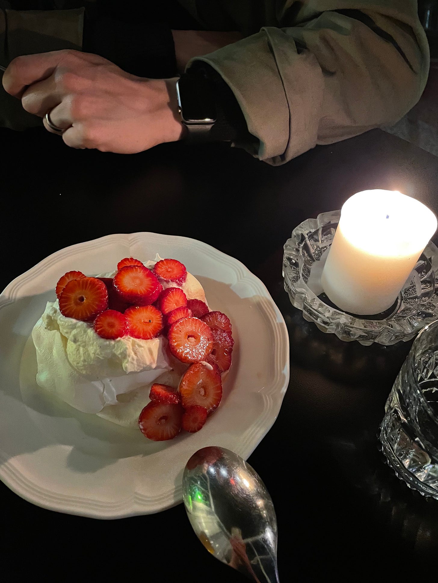 Small pavlova on a white plate with fresh cream and sliced strawberries soaked in pet nat.