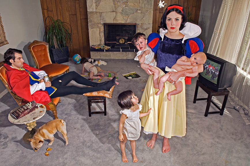 Staged photo of Snow White standing in the middle of a suburban living room holding two children in diapers, one crying, one sucking her thumb. Another daughter pulls on her skirt, while a fourth is crawling in a corner of the room. bulldog sniffs the floor. Her princely husband sits on a chair, watching TV and holding a can of beer.