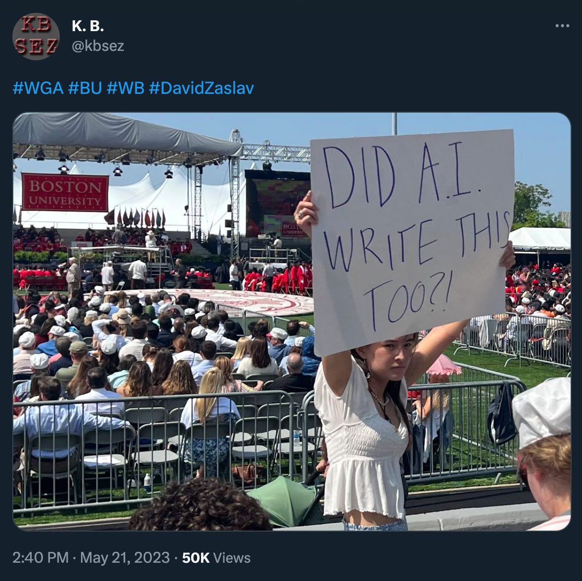 A young woman holds up a hand-drawn sign at the BU graduation that reads “DID A.I. WRITE THIS TOO?!”