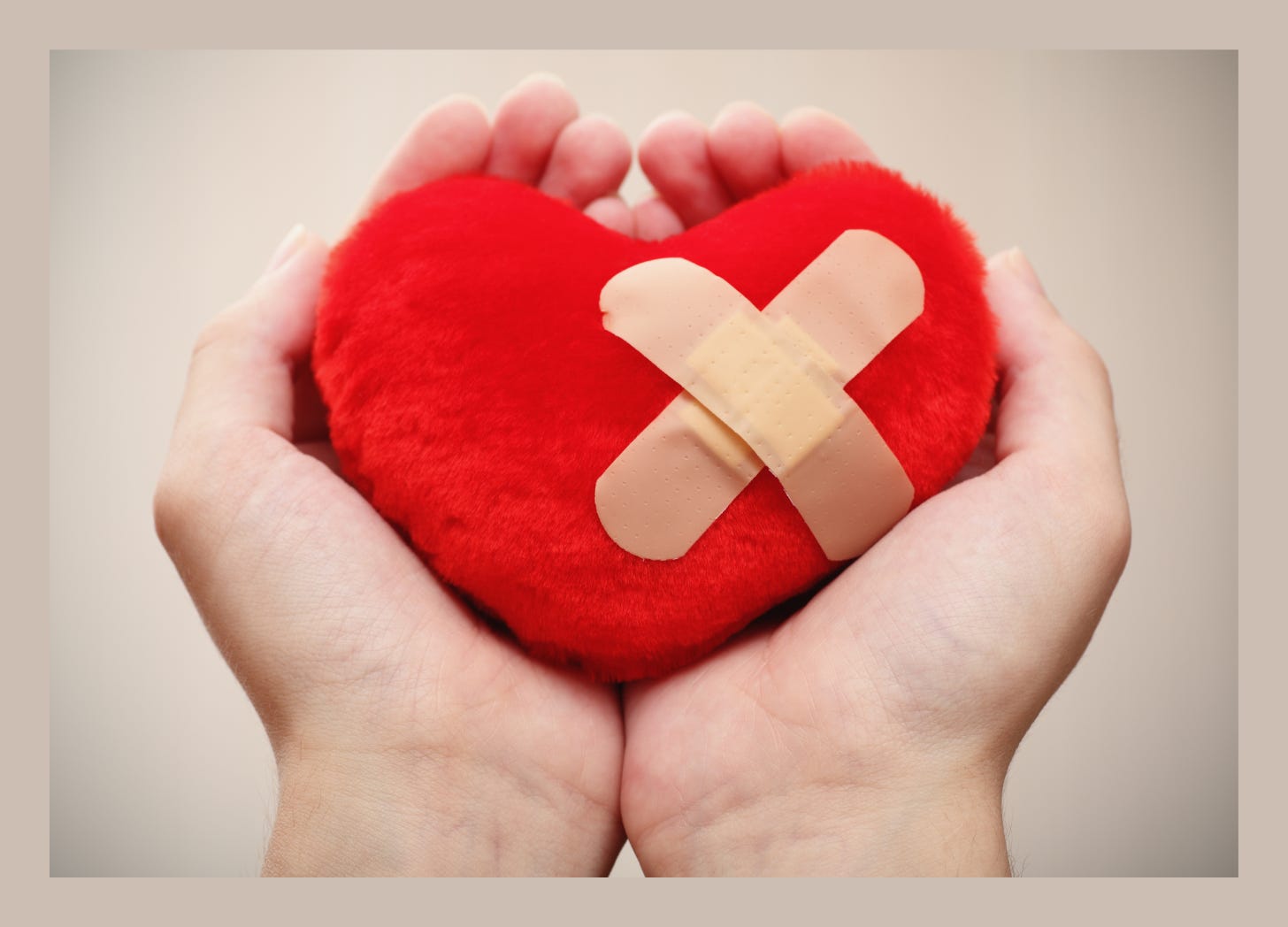 Hands cradling a red heart with Band-Aids on it