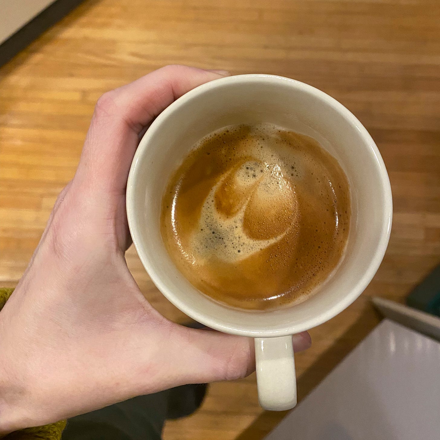 From above, my hand holding a mug of espresso. In the crema is an attempt at a design as described above.