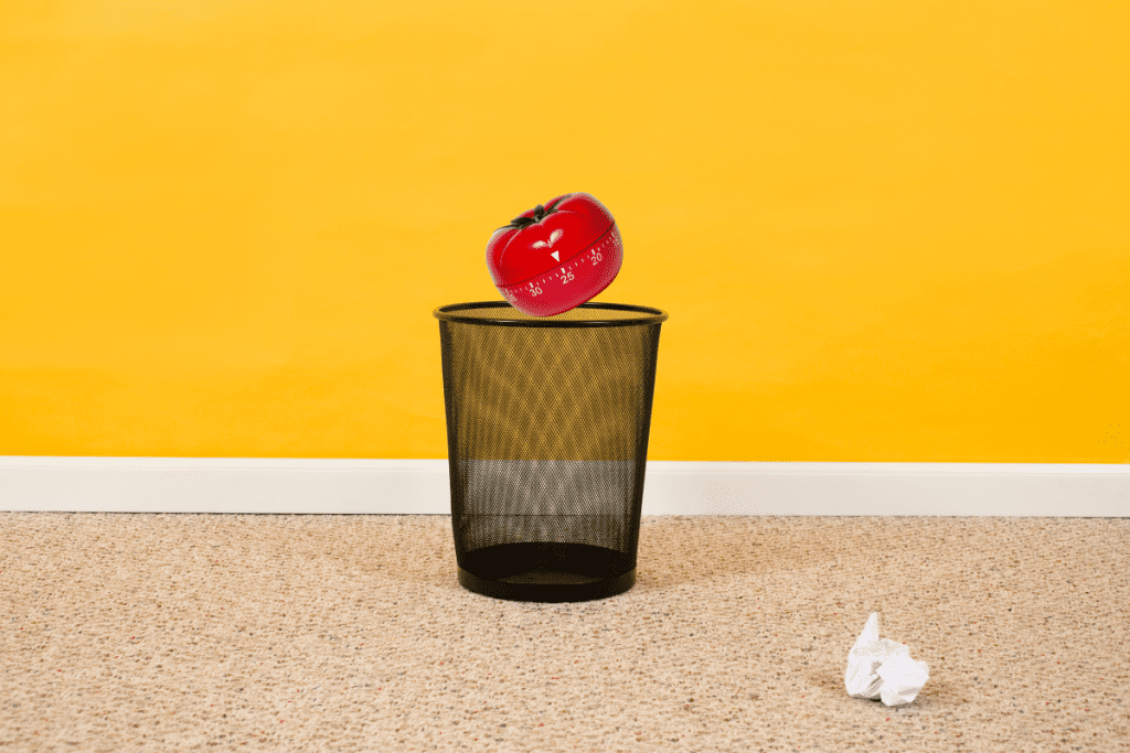 Pomodoro tomato timer being dropped into empty wastebasket to achieve focused thinking