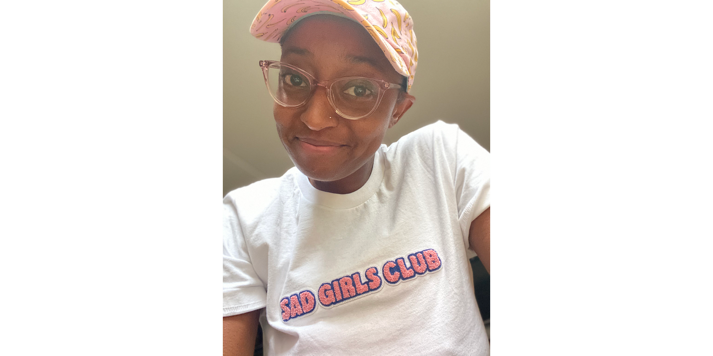 Ashley wearing a pink banana cap, pink sunglasses, and a t-shirt that says "SAD GIRLS CLUB"
