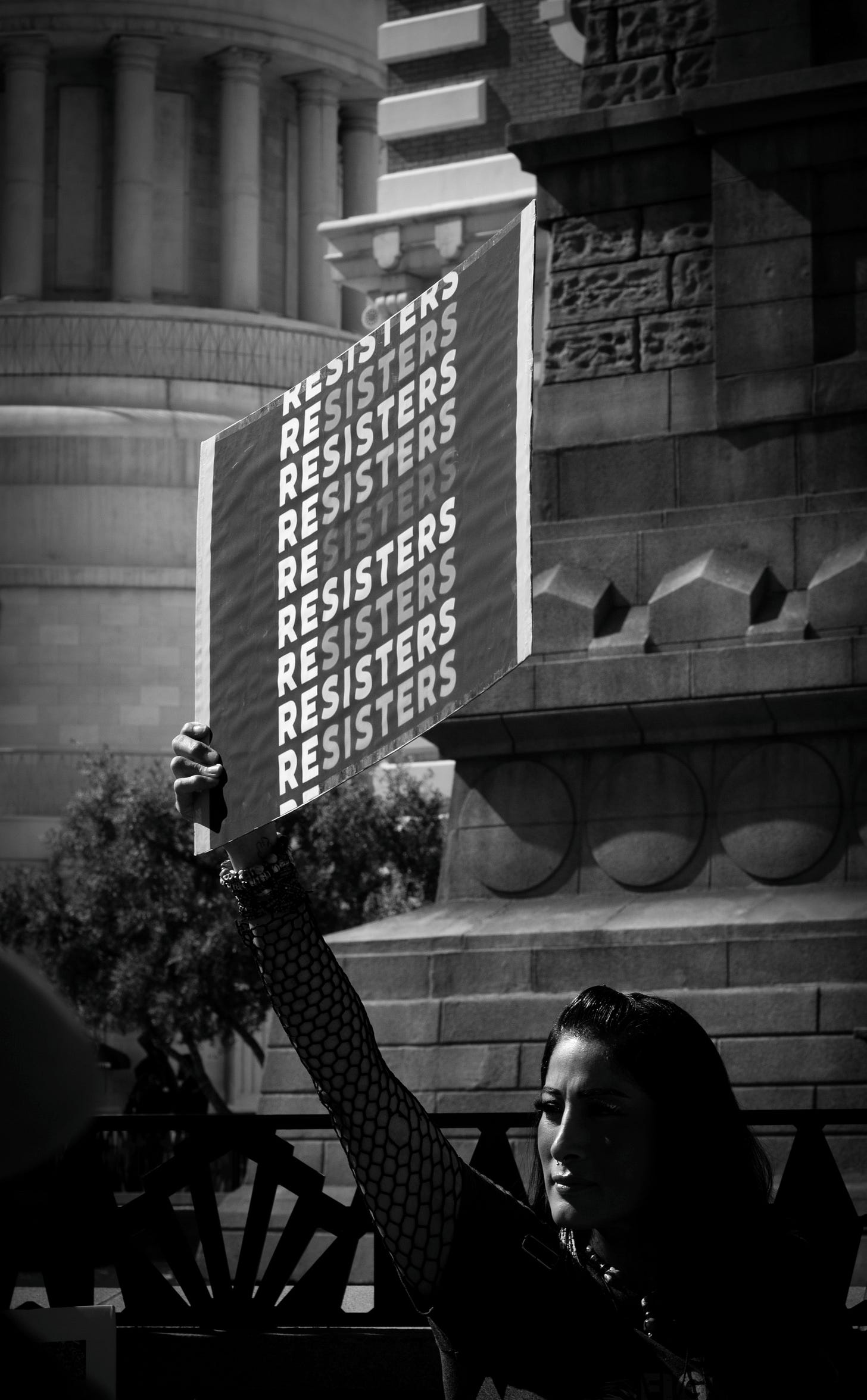 Black and white image of a women holding a sign that repeats "Resister."