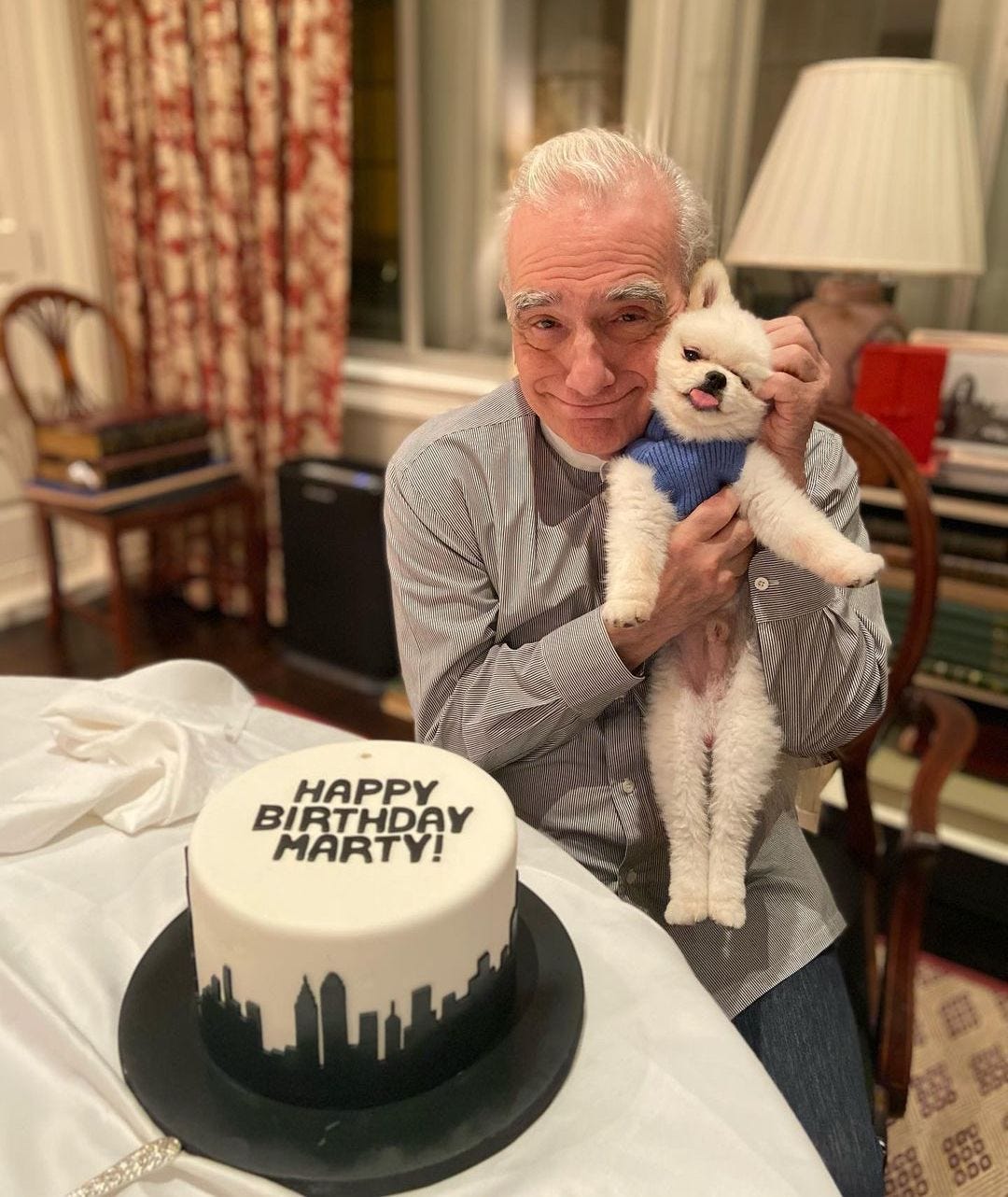 Martin Scorsese holding a small dog to his face and sitting next to a birthday cake.