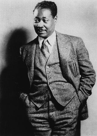 Claude McKay, standing in a suit with his hands in his pockets.