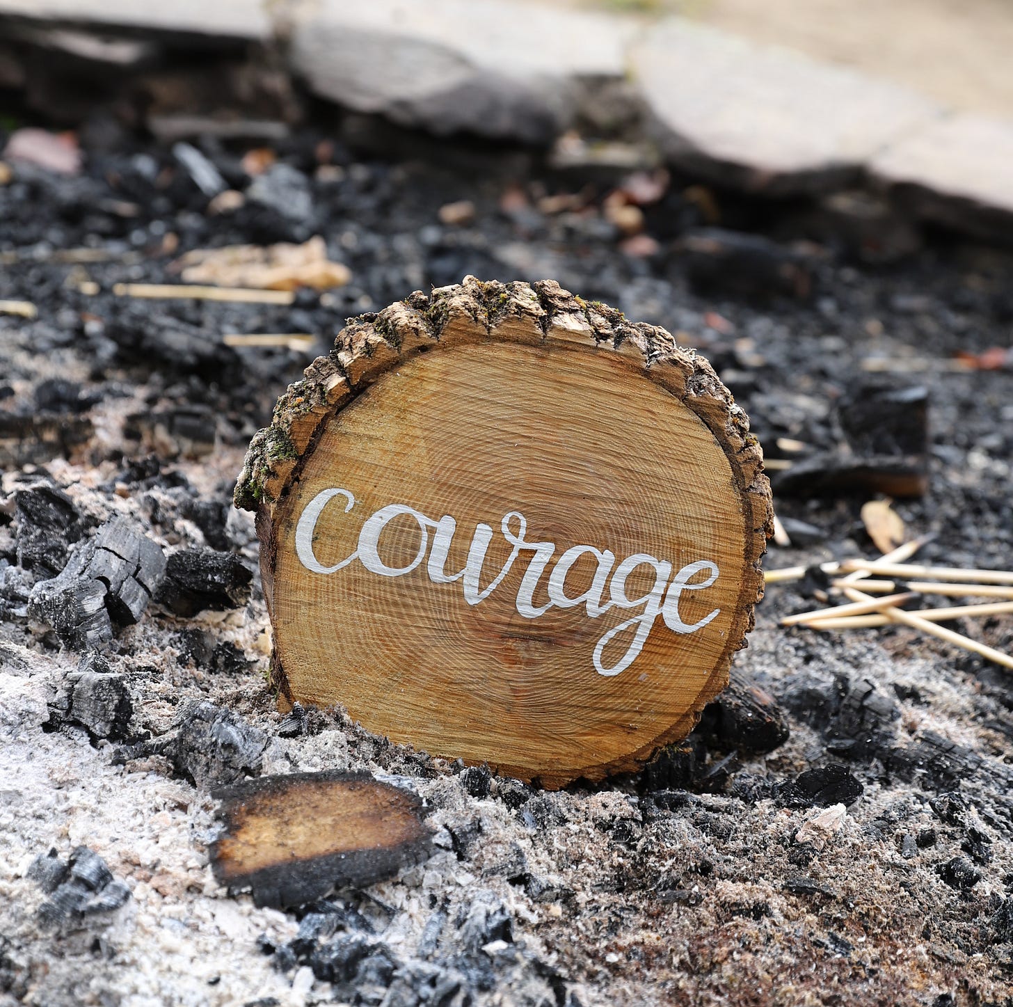 A piece of wood with the word "courage" burned into it rests amid glowing embers in a smoldering firepit, symbolizing resilience and strength through adversity. A piece of wood with the word "courage" burned into it rests amid glowing embers in a smoldering firepit, symbolizing resilience and strength through adversity.