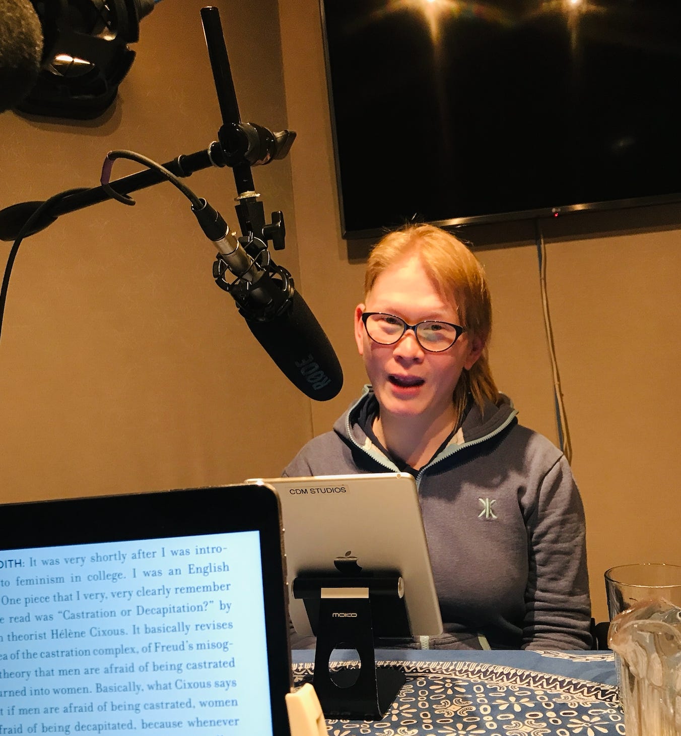 Meredeth Talusan in a recording booth. In front of her is an iPad and a microphone. 