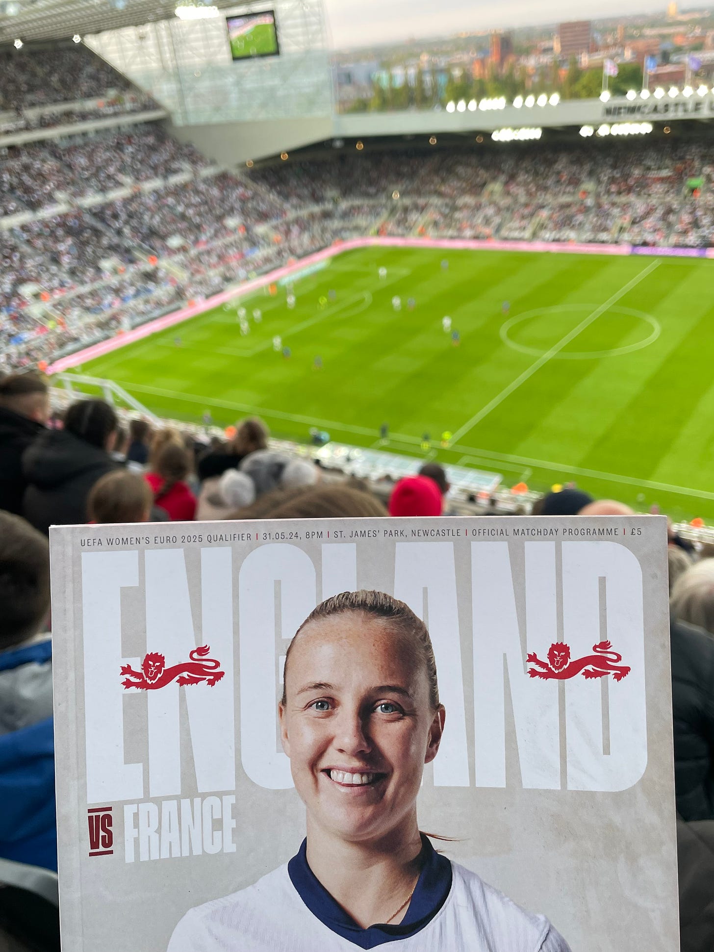 In the foreground is the programme for the England vs. France women's match. The background is the view from our seats at St. James Park, over the pitch and the stand opposite.