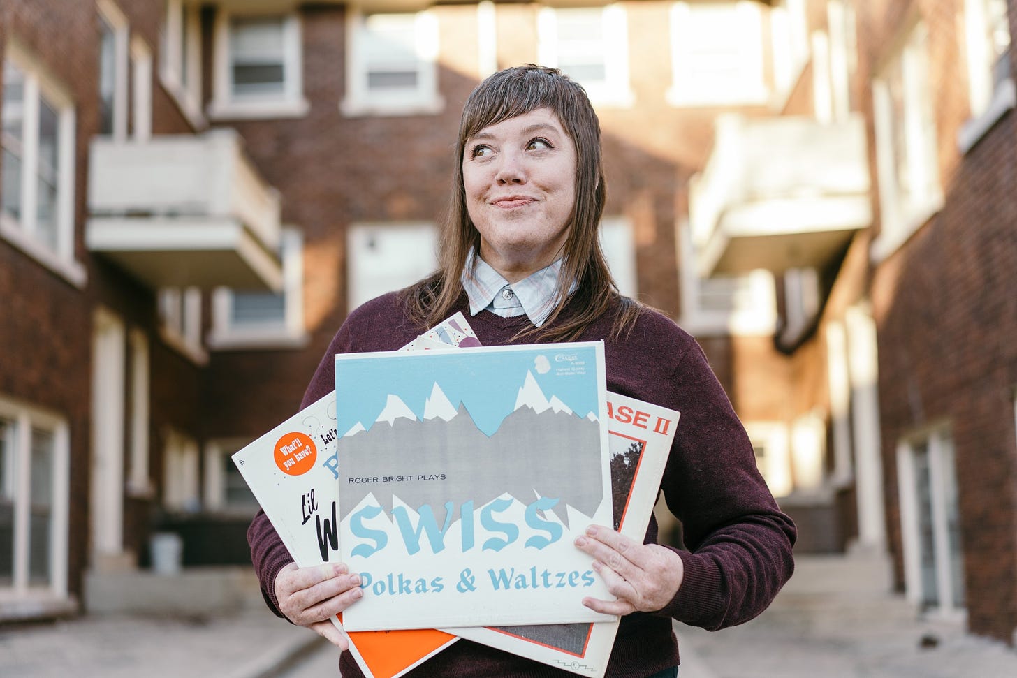 Stacy holding three polka vinyl records, smiling and looking off to the side