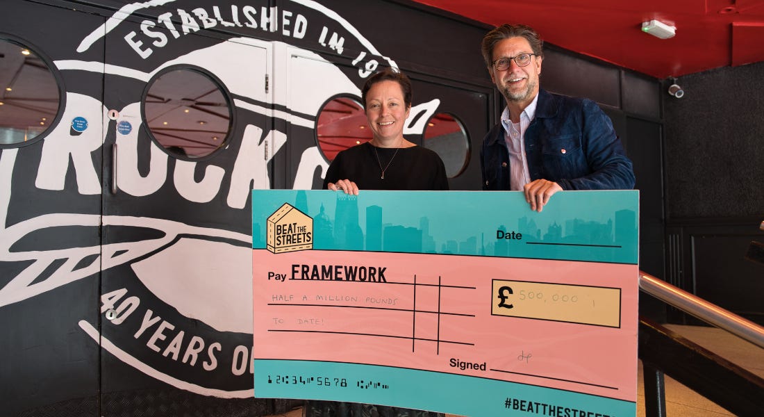 A man and a woman holding a blue and pink large cheque, in front of a black and white door with the Rock City logo A man and a woman holding a blue and pink large cheque, in front of a black and white door with the Rock City logo