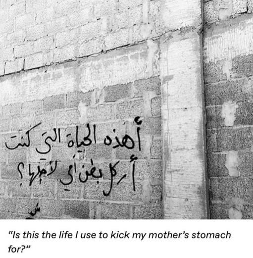 a greyscale image of black graffiti on a brick wall. the graffiti reads (in arabic): “is this the life i used to kick my mother’s stomach for?”