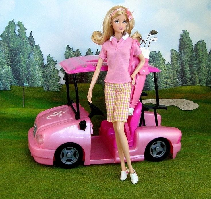 Barbie doll dressed in pink golf gear with golf clubs and pink buggy on a golf course