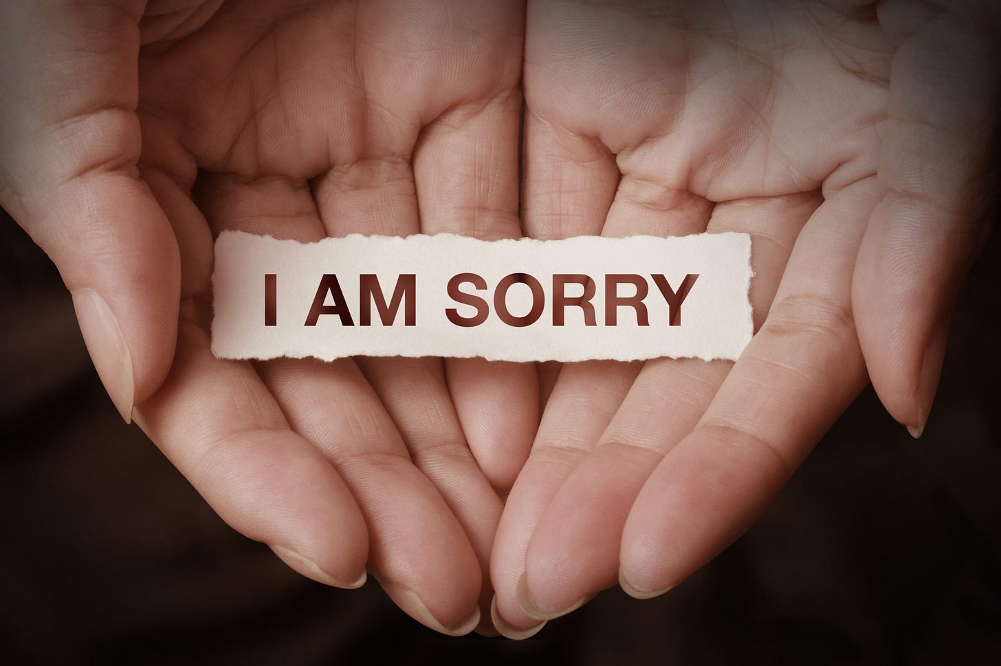 A pair of cupped hands holding a small scrap of paper which reads I AM SORRY