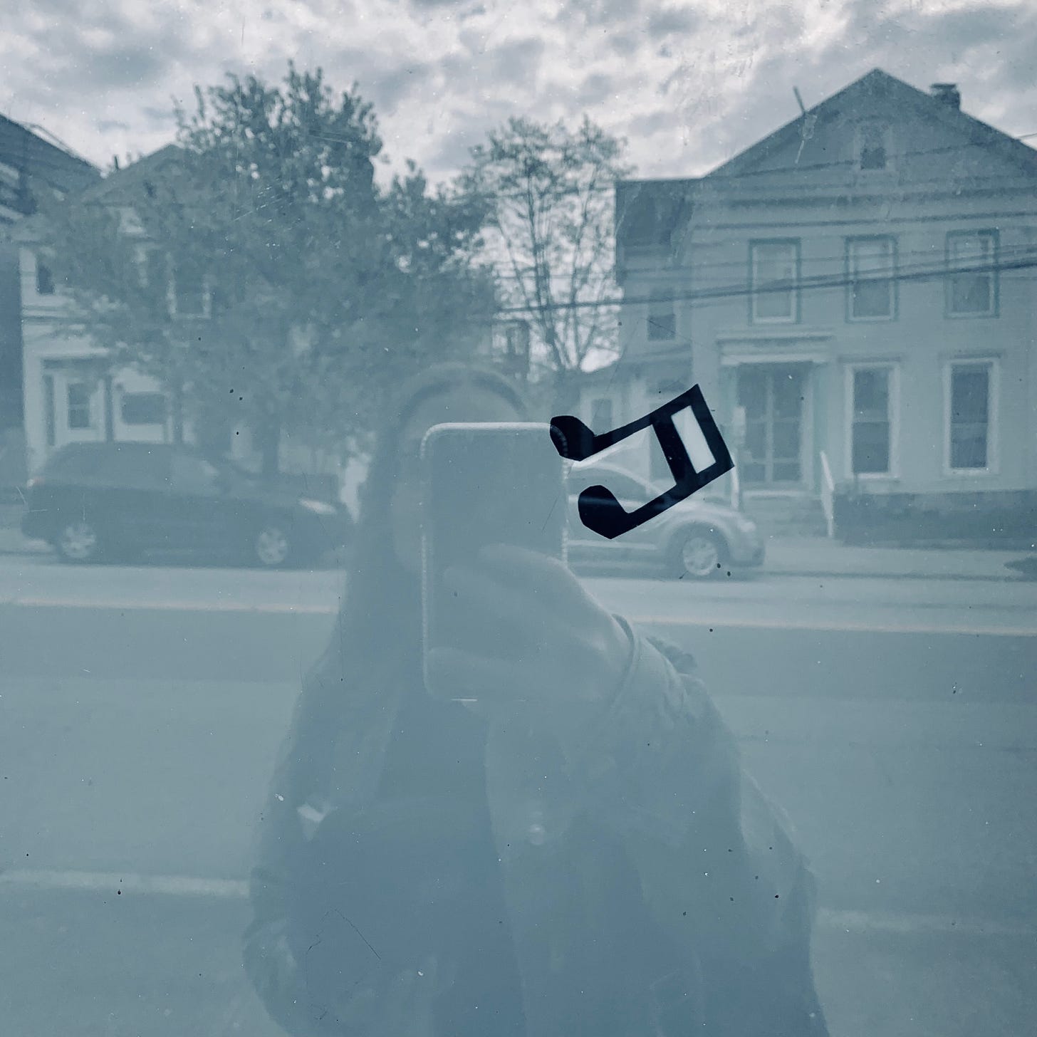 A woman taking a photo of her reflection in a display window, which is empty except for a single music note